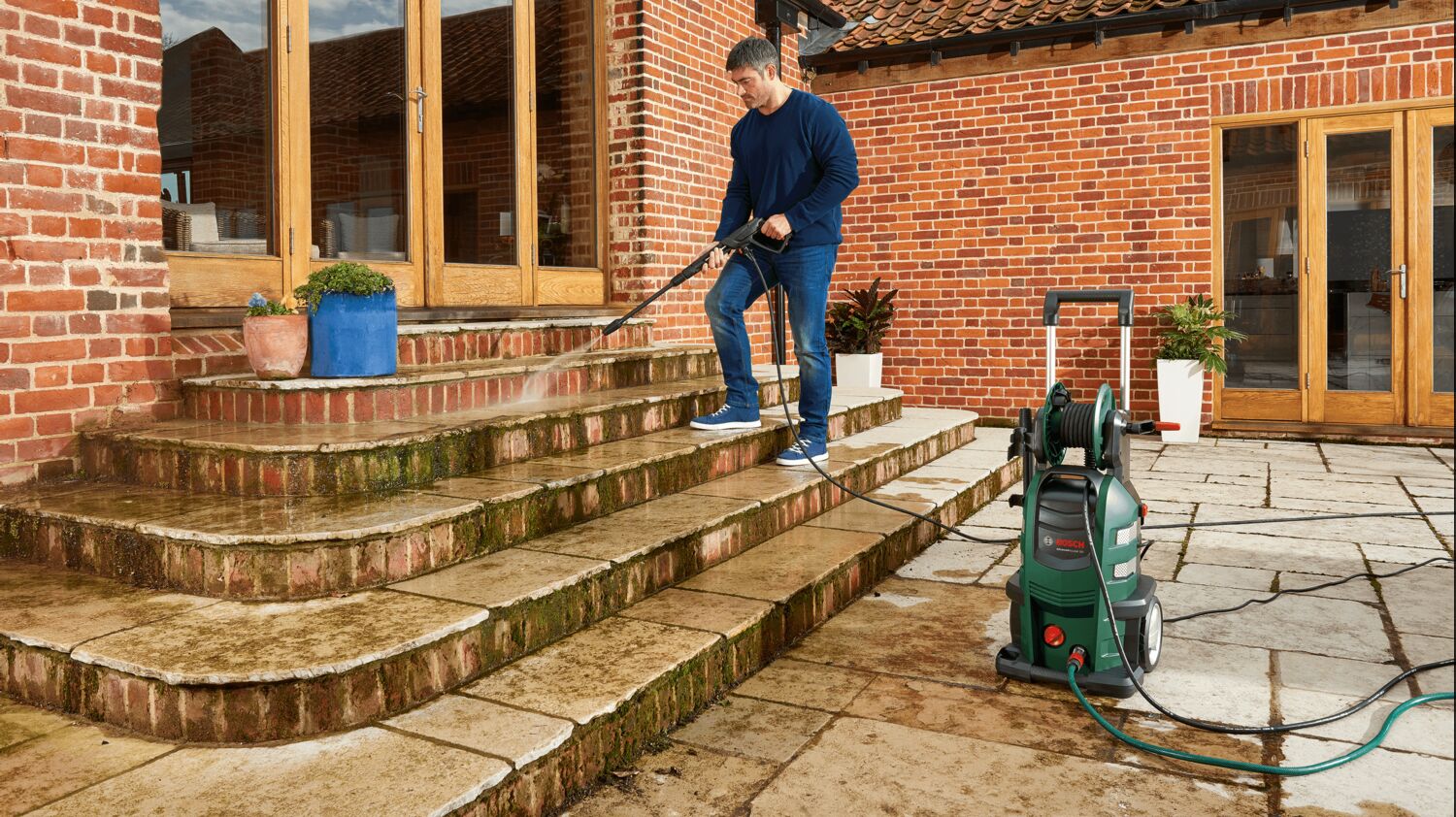 Bosch AdvancedAquatak 160 junto a unos escalones de ladrillo mientras una persona limpia el musgo acumulado