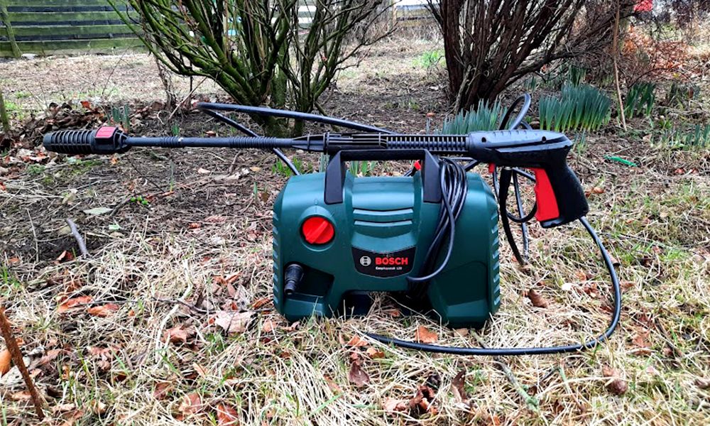 Bosch EasyAquatak 120 apoyada sobre el césped de un jardín, con la lanza y la pistola desplegadas