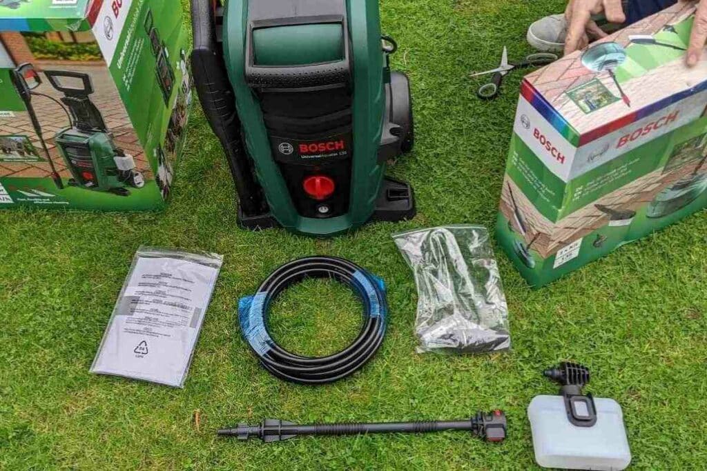 Bosch UniversalAquatak 135 recién desembalada sobre el césped, con manguera, lanza y cajas originales alrededor