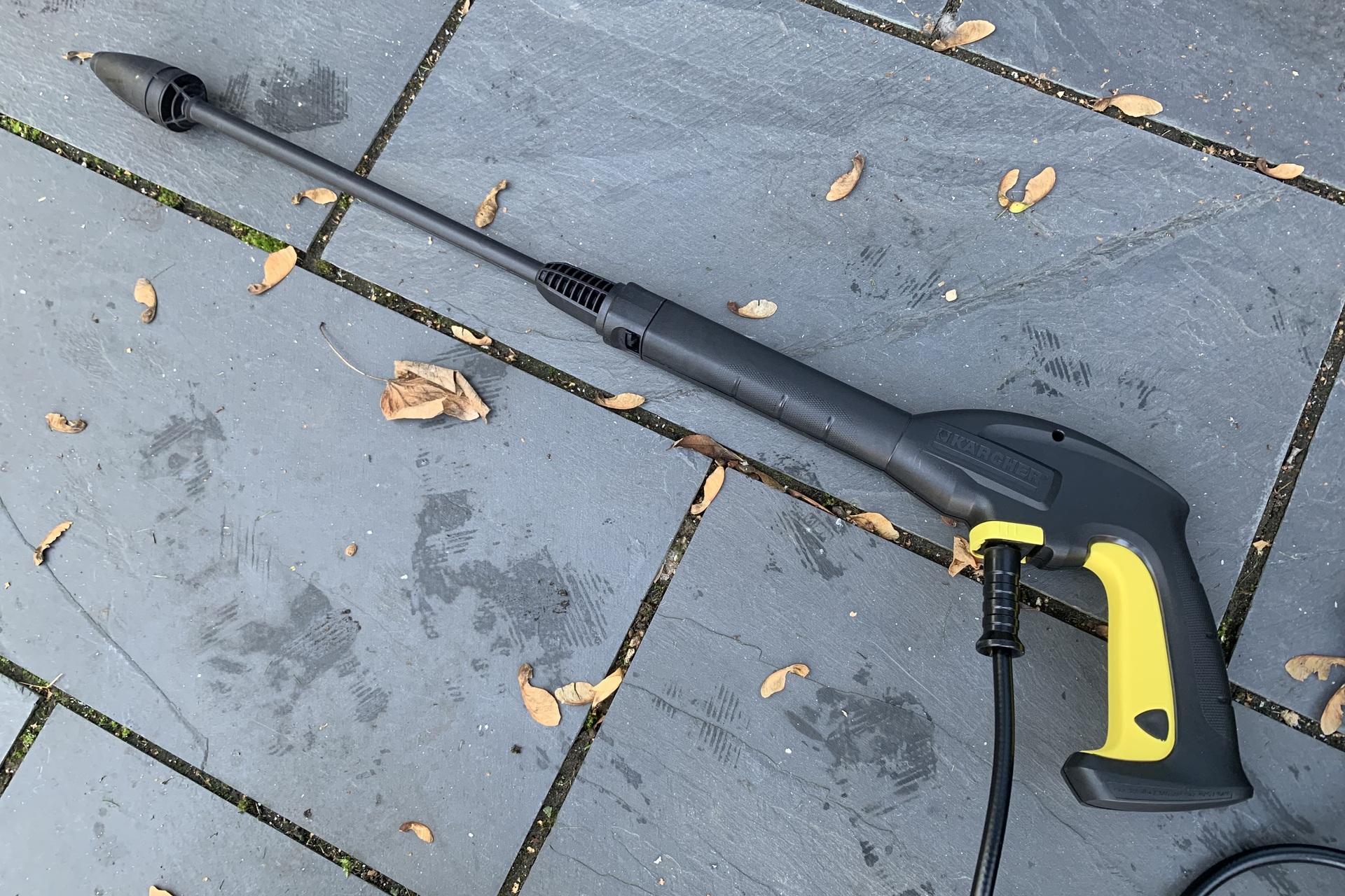 Pistola y lanza de la Kärcher K2 sobre una terraza de piedra, con la manguera de alta presión enrollada al fondo