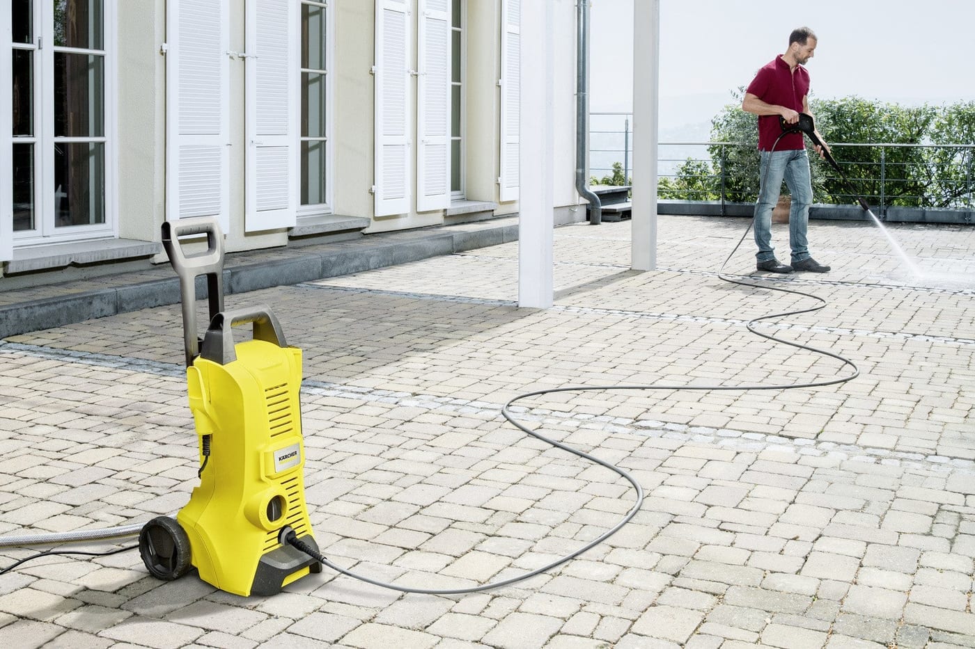 Kärcher K3 limpiando una terraza de adoquines con visible línea de suciedad y limpieza